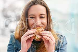 Quick snack then back to the fun. Portrait of a beautiful young woman eating a sandwich at an amusement park outside.