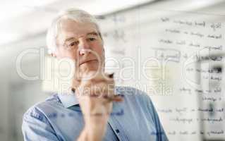 Ideas are the foundation of any business. a senior businessman writing down ideas with a pen marker on a glass wall in the office.