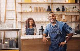 Youve come to the right place for coffee. a handsome young businessman standing in his cafe while a barista works behind him.