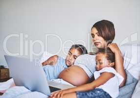 Spending a nice day inside with the kids. two focused little girls relaxing next to their pregnant mother while watching a movie on a laptop at home during the day.