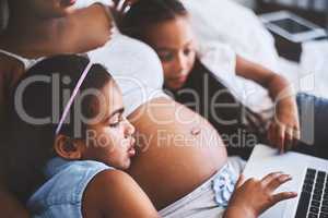 Next movie. two focused little girls relaxing next to their pregnant mother while watching a movie on a laptop at home during the day.