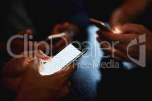 Texting everyone to come and join us. Closeup of a group of unrecognizable people texting on their phones while being seated inside of a bar at night.