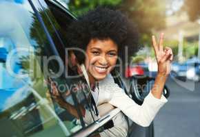 On my way to work finally. Portrait of a cheerful young businesswoman driving in a car to work while leaning out of the vehicle and showing the peace sign.