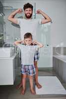 Check out these babies. Portrait of a father and his little son flexing their arms in the bathroom at home.