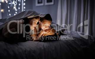 Technology is simply a part of their upbringing. two adorable little siblings using a digital tablet together in bed at night.