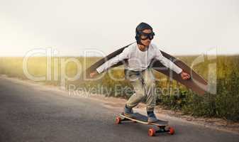 Have you seen a kid any cooler. a young boy pretending to fly with a pair of cardboard wings while riding a skateboard outside.