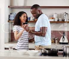 I love his random romantic gestures. a young married couple dancing in the kitchen at home.