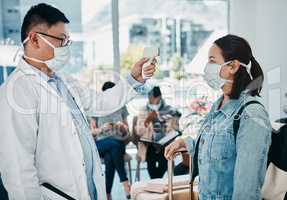 Covid traveling with a doctor taking temperature of a woman wearing a mask in an airport for safety in a pandemic. Healthcare professional with an infrared thermometer following travel protocol