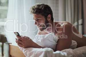 Wake up then check up on my social media. a handsome young man using a cellphone at home.