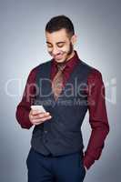 Technology has become part of becoming successful in business. Studio shot of a handsome young businessman using a cellphone against a grey background.