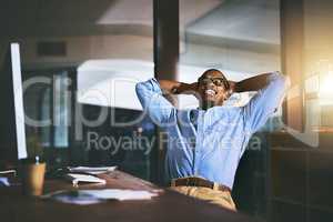 Beating deadlines like a boss. a handsome young businessman relaxing at his desk during a late night at work.
