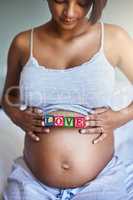 So much love for my little one. a young pregnant woman with wooden blocks on her belly that spell the word love.