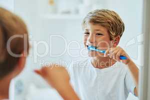 Brushing your teeth is an important routine. a cheerful young boy looking at his reflection in a mirror while brushing his teeth in the bathroom at home during the day.