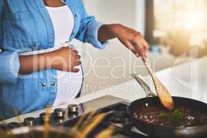 Some home cooked loving for baby bump. a pregnant woman preparing a meal on the stove at home.