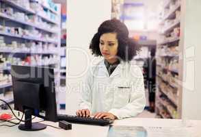 She works hard to get her customers the lowest prices. a pharmacist working on a computer in a pharmacy.