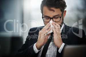 I cant deal with getting sick right now. a young businessman blowing his nose in an office.
