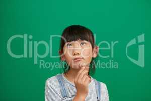 What should I do today. Studio shot of an adorable little girl standing and contemplating against a green background.