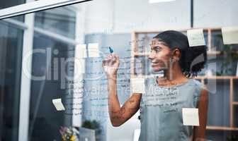 Female leadership and marketing professional brainstorming innovation ideas, writing on transparent board with sticky notes in office. Young entrepreneur planning business mission and strategy.