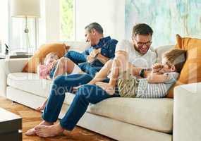 Getting their daily dose of tickles. Full length shot of an affectionate family of four on the sofa at home.