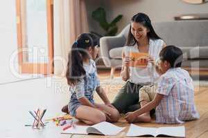 Think hard and carefully. a cheerful mother and her two children doing homework together while seated on the floor at home during the day.