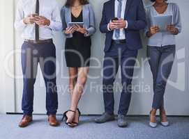 Keeping up with the pace of business. a group of unrecognizable businesspeople using wireless technology while standing against a grey background.