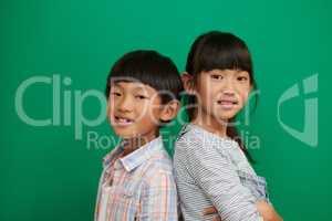 Brothers and sisters should stick together. Studio portrait of two cheerful children standing with their backs against each other next to a green background.