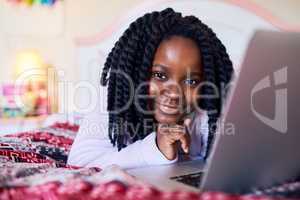 Tech savvy at a young age. an adorable little girl using a laptop while lying on her bed in her bedroom.