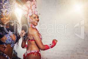 Dancing has always been part of their lives. Portrait of two female dancers wearing vibrant costumes while dancing to music inside of a busy nightclub.