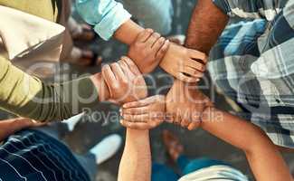 We will never let go. High angle shot of a young group of work colleagues forming an unique huddle with their arms and hands while standing in the office at work.