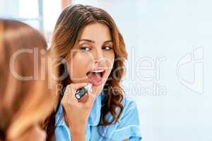 Make up enhances your beautiful features. a beautiful young woman applying lipstick at home.