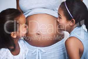 Cuteness overload. two cheerful little girls standing next to their mother and giving her pregnant belly a kiss at home during the day.