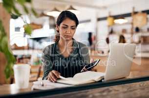 Cafe owner with laptop, phone and book checking online order, searching available bookings and preparing takeaway deliveries coffee shop. Serious local restaurant entrepreneur pricing a menu on tech