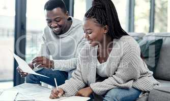 Happy African American couple doing finance planning, writing budget paperwork on sofa at home. Smiling boyfriend and girlfriend discussing insurance bills, savings and investments for future.