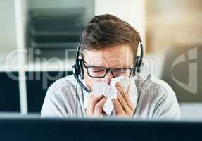 Hope Im not getting sick again. a young call centre agent blowing his nose while working in an office.