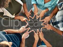 Lets see what it means to be a team. High angle shot of an unrecognizable group of work colleagues forming an unique huddle with their fingers while standing in the office at work.