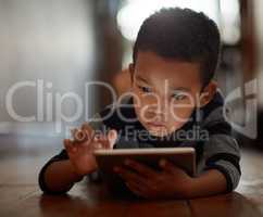 Exploring a world of apps. a young boy using his digital tablet while lying on the floor at home.