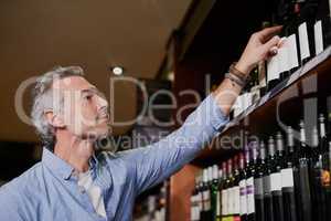 He knows a good vintage when he sees one. a handsome mature man buying wine at a grocery store.