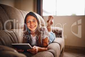 I like to spend a little time online everyday. Full length portrait of a young girl using her tablet while lying on a sofa at home.