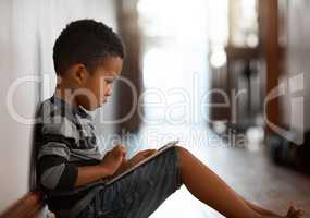 Exploring the world from a corridor at home. a young boy using his digital tablet while sitting on the floor at home.