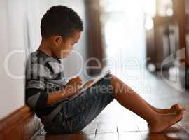Technology is all-inclusive. Full length shot of a young boy using his digital tablet while sitting on the floor at home.