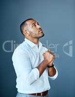 When business looks down, start looking up. Studio shot of a young businessman looking up with his hands clasped in prayer.
