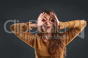 Being silly today. Studio portrait of a cheerful young woman making a face with her hands while standing against a dark background.