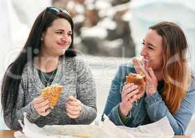 Were here to eat and have fun. two female best friends eating sandwiches at an amusement park outside.