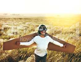 Let their imaginations take flight. a young boy pretending to fly with a pair of cardboard wings in an open field.