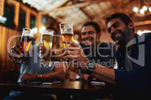 How many have we had now. a group of young friends seated at a table together while enjoying a beer and celebrating with a celebratory toast inside a bar.