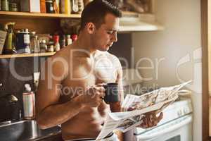 Getting his daily intake of caffeine and news. a handsome young shirtless man drinking a cup of coffee and reading the newspaper in the kitchen at home.