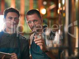 That beer there is our pride and joy. two young working men doing inspection of their beer making machinery inside of a beer brewery during the day.