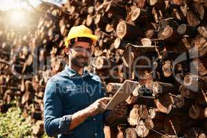 Hes the man for all your lumber needs. a lumberjack using his tablet while standing in front of a pile of wood.
