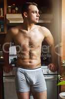 The morning is a great time for contemplation. a handsome young shirtless man in the kitchen at home.
