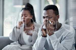 Flu, cold or sick couple with covid coughing, sneezing and blowing their nose with a tissue while in isolation together at home in winter. Young husband and wife with a bad seasonal fever illness